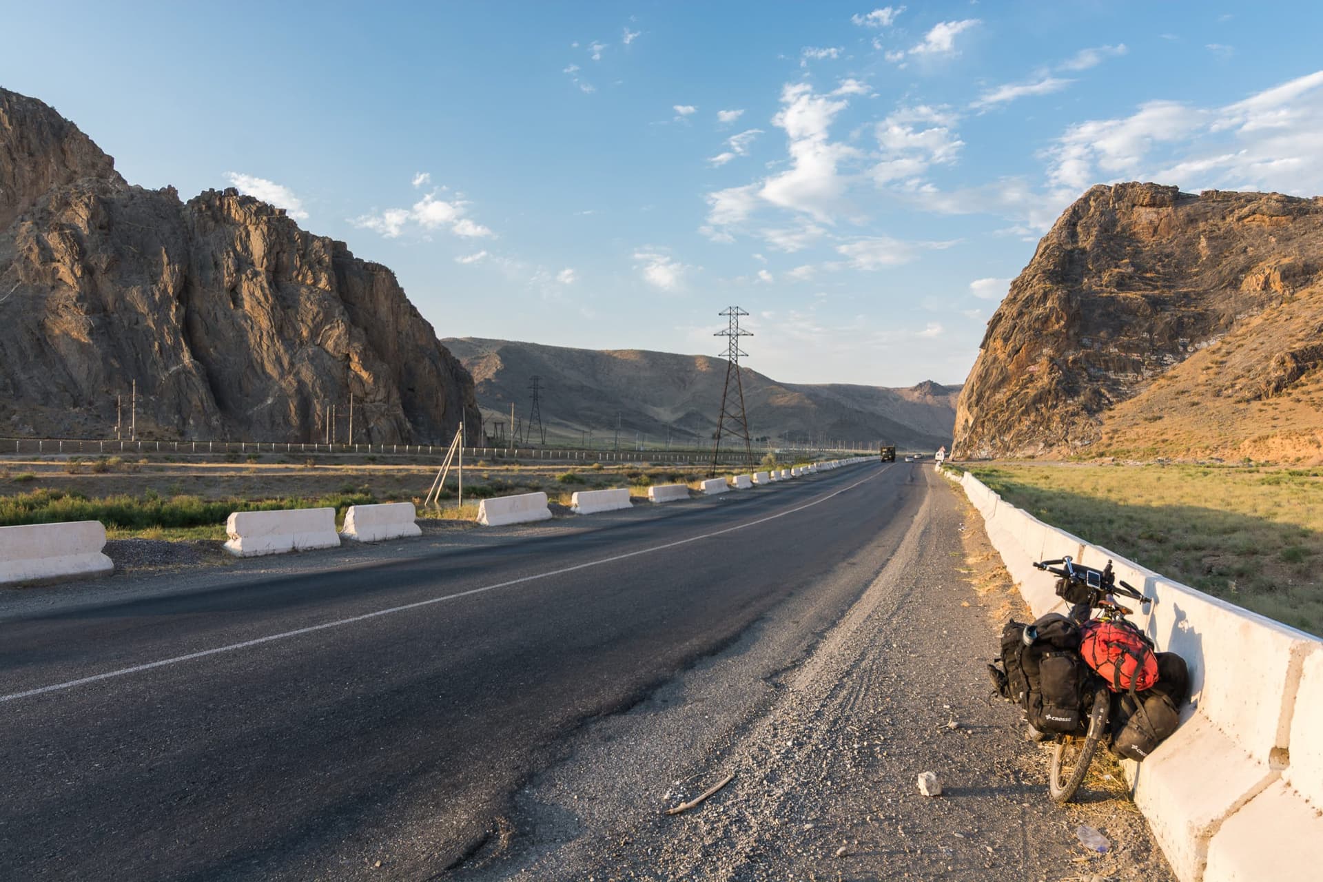 Bicicleta cargada apoyada en la mediana de una carretera entre montañas rocosas de Uzbekistán